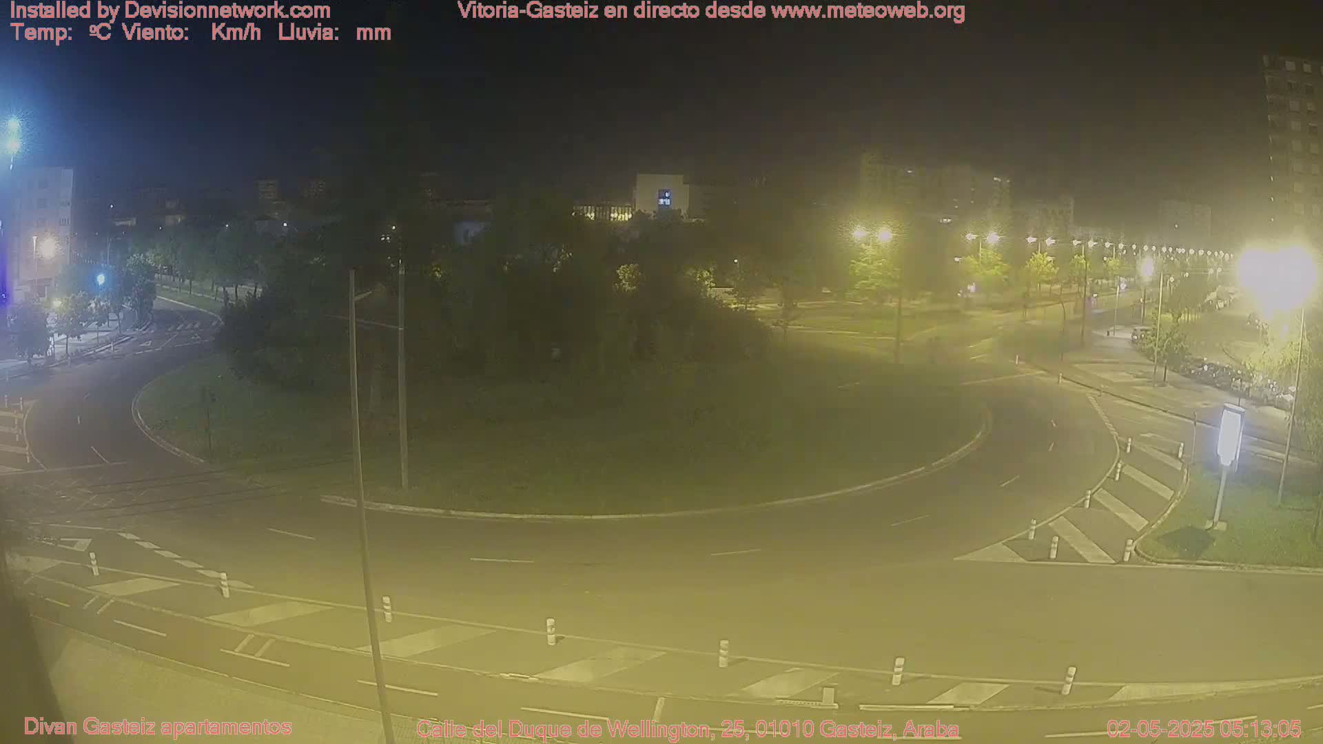 A nighttime view of a roundabout and surrounding streets illuminated by streetlights, with some buildings visible in the background.