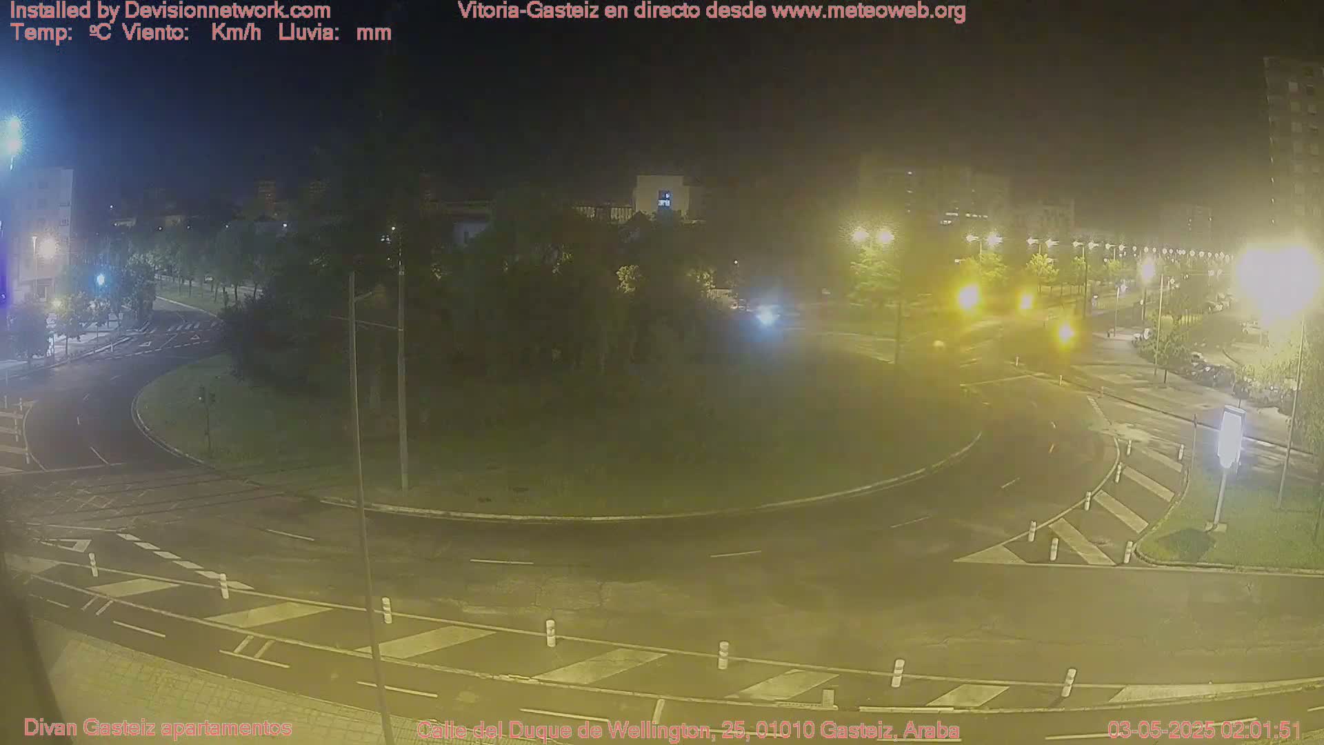 A nighttime view of a wet roundabout and surrounding streets illuminated by streetlights.