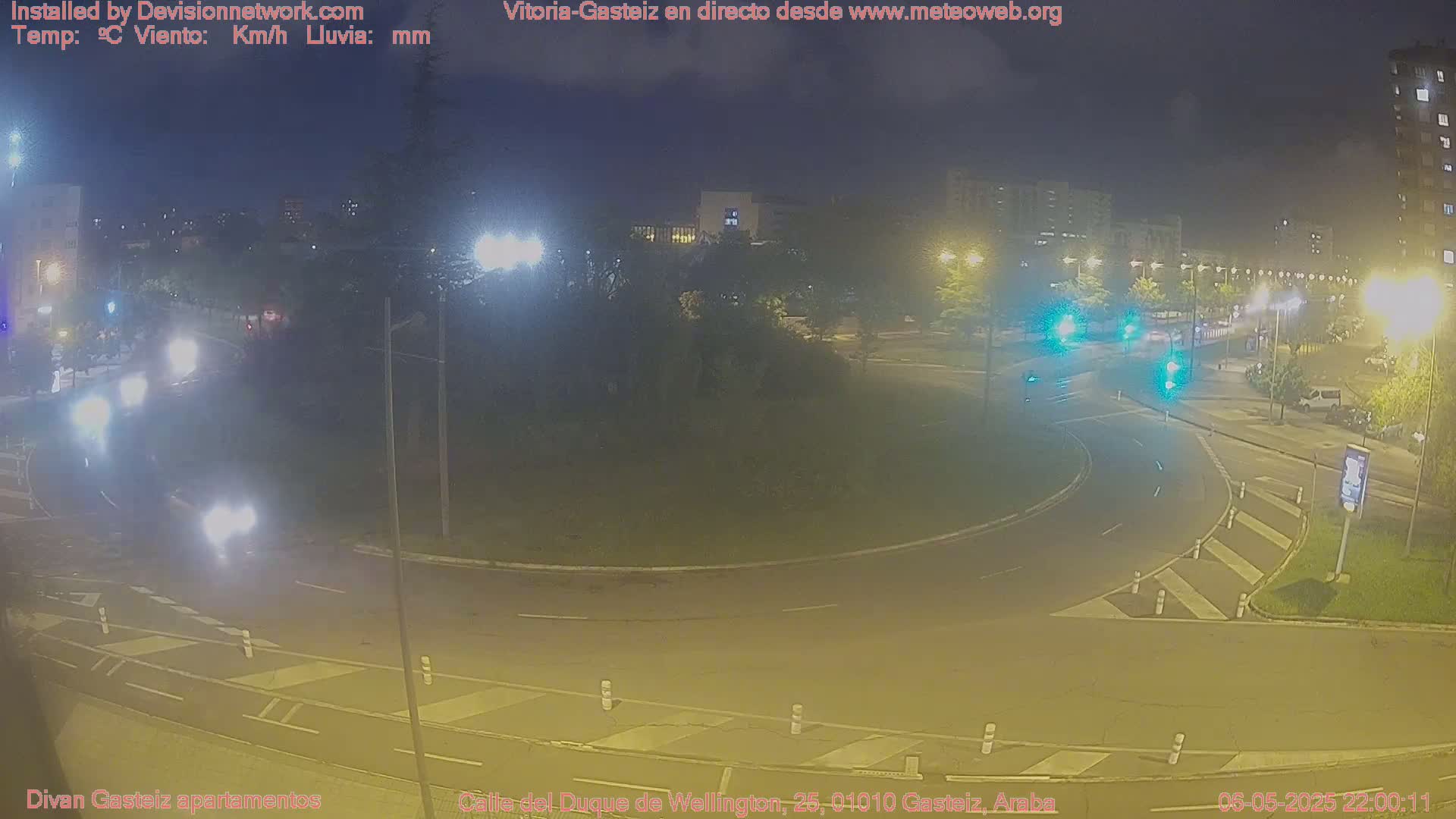A nighttime view of a traffic circle with several vehicles and streetlights illuminated, under clear skies.
