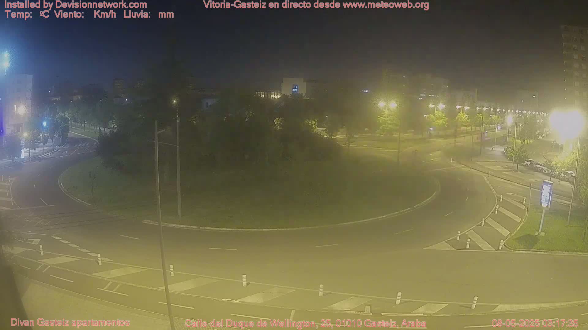 A nighttime view of a roundabout with cars and streetlights, under hazy conditions.