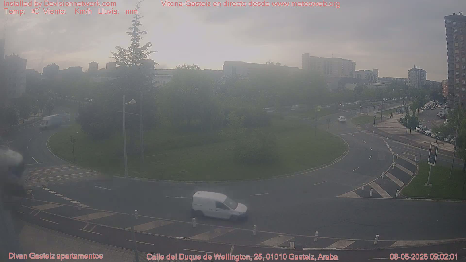 A hazy view of a roundabout and surrounding city streets, with a white van driving on the roundabout.