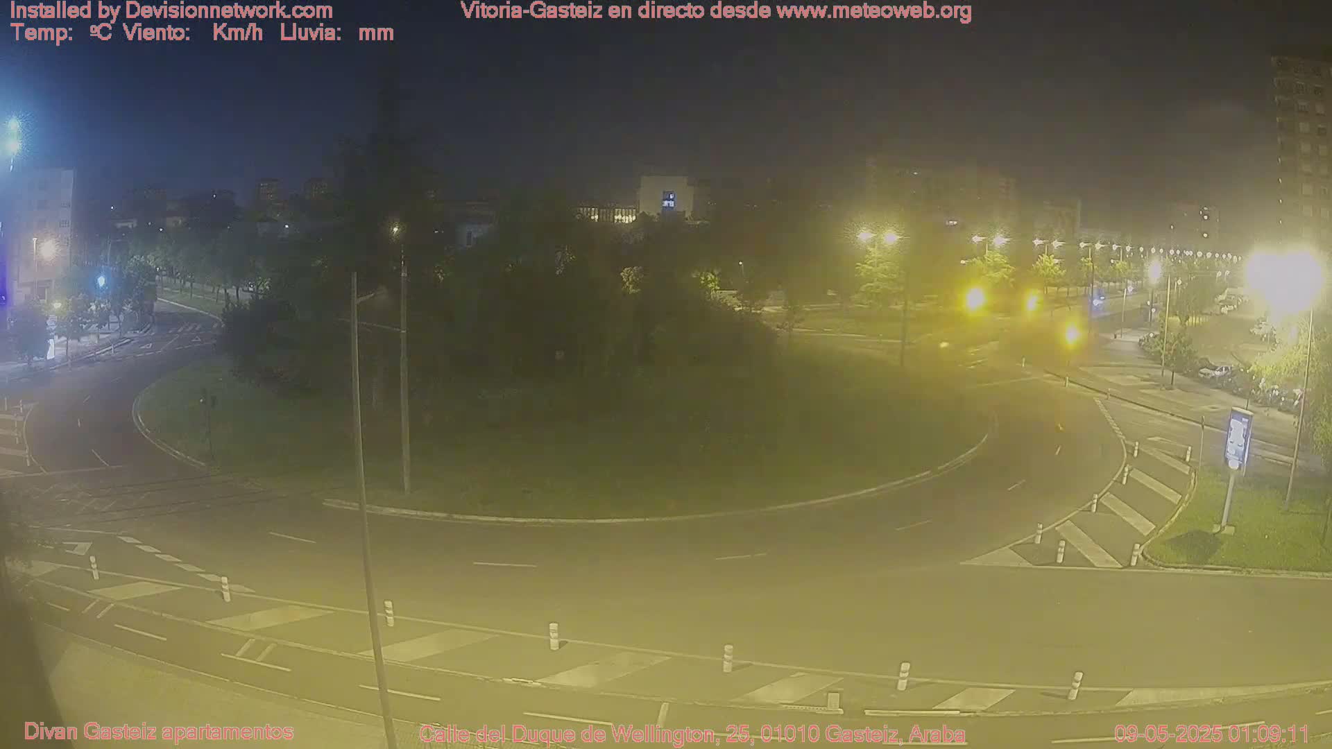 A nighttime view of a roundabout with surrounding streets and buildings under hazy, yellow-toned lighting.