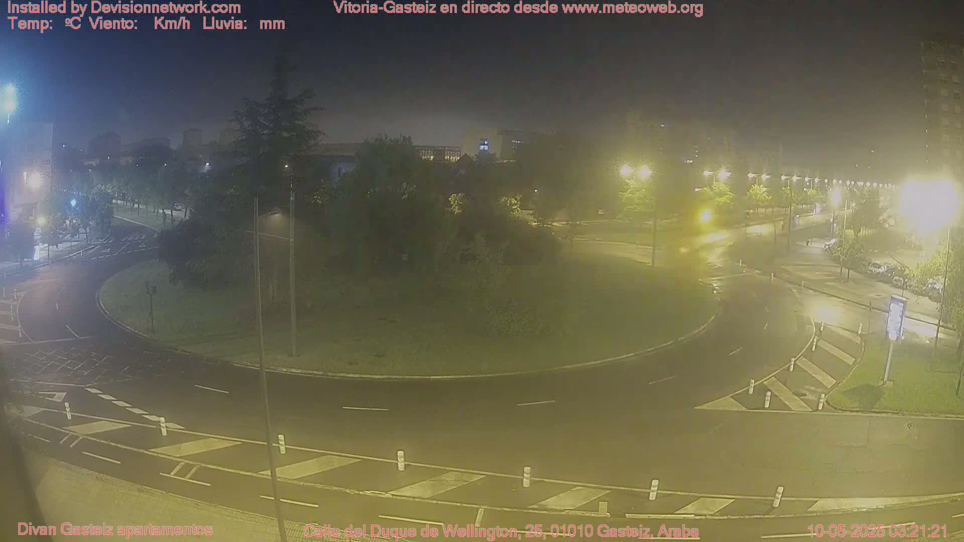 A nighttime view of a wet roundabout and surrounding streets, illuminated by streetlights.