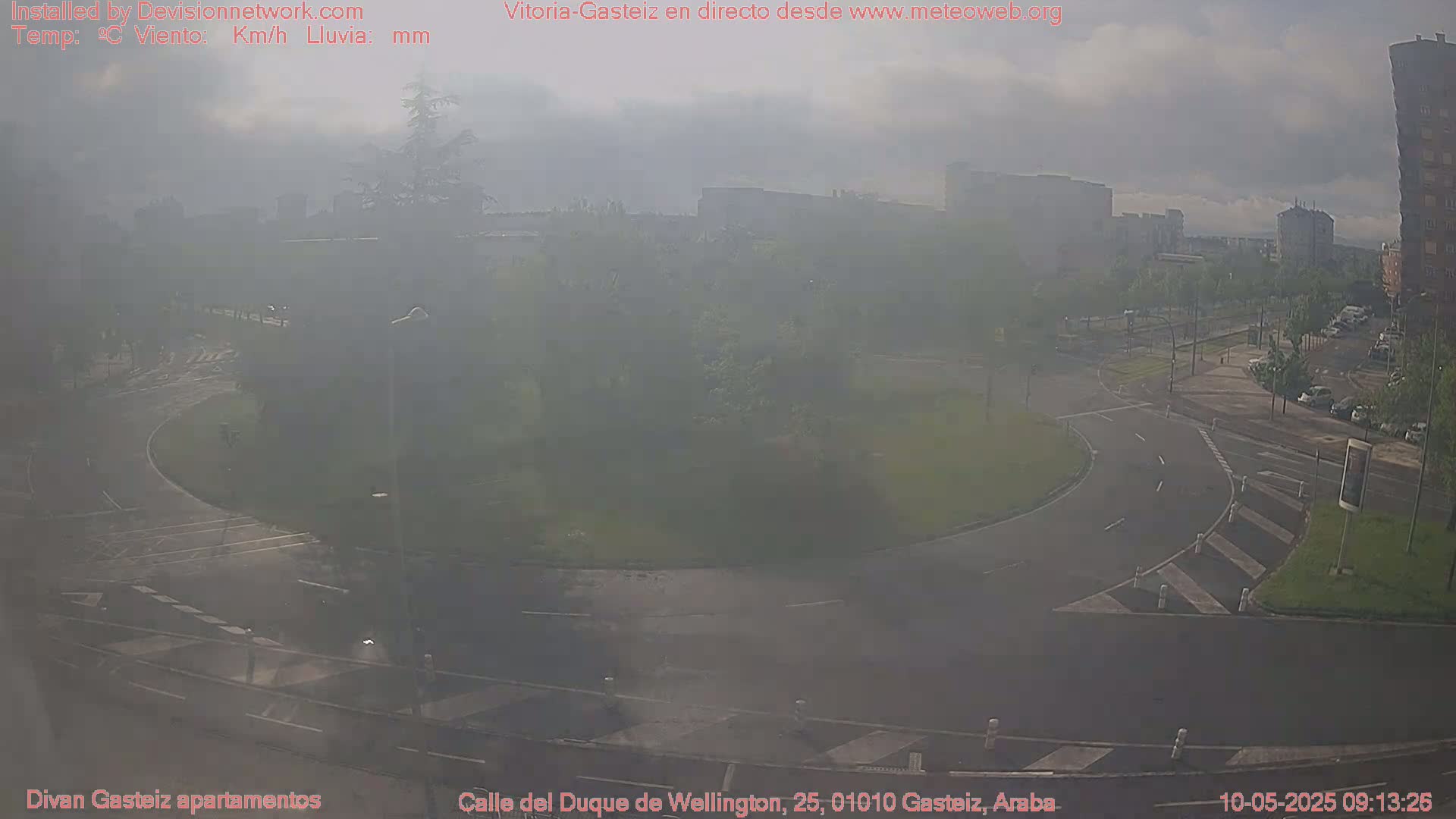 A hazy, overcast day reveals a roundabout intersection surrounded by buildings and greenery.