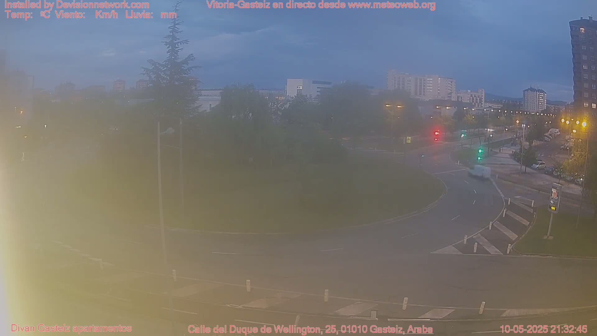 A mostly empty roundabout with several vehicles and buildings visible in the dusky evening light.