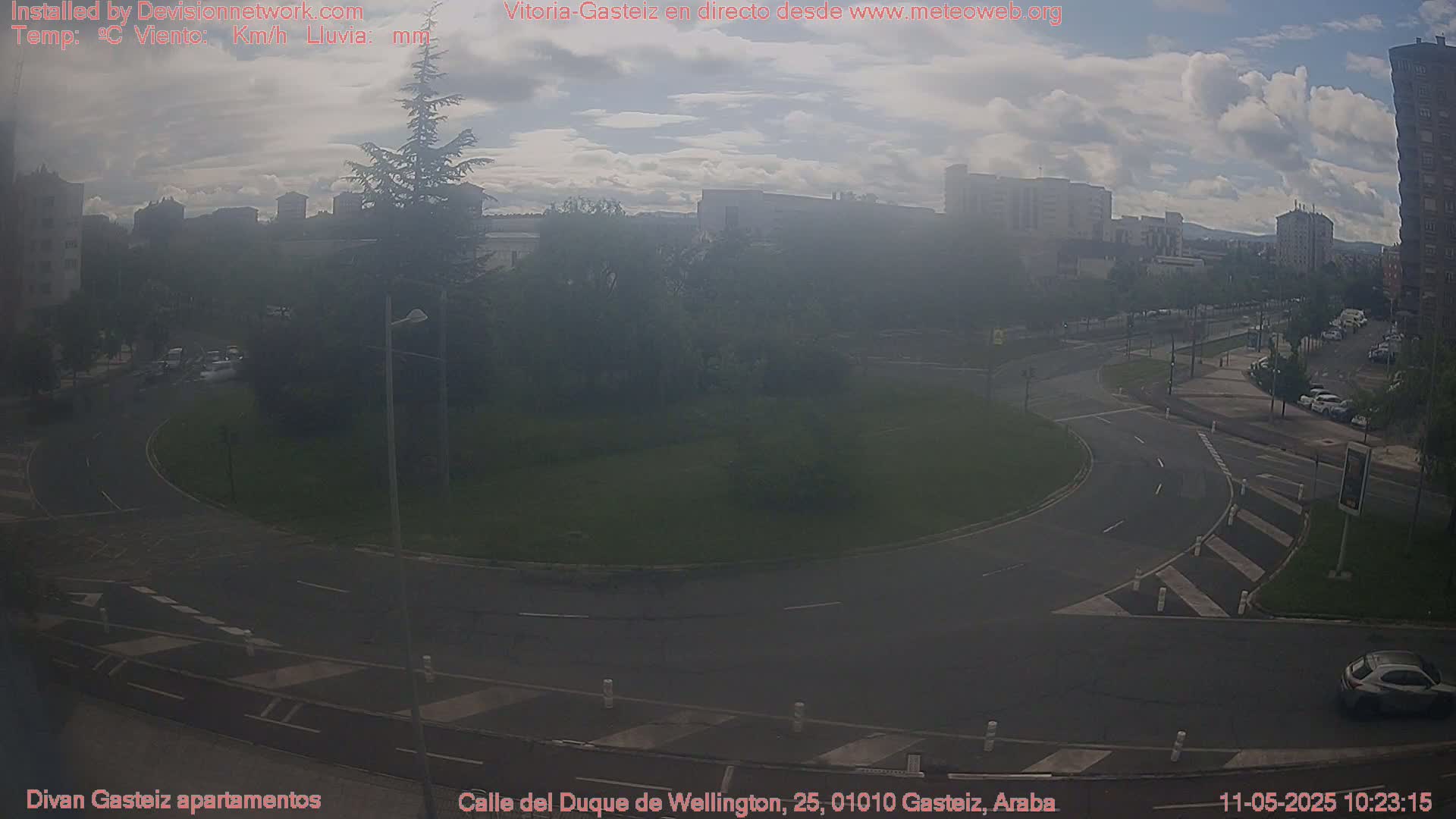 A hazy, overcast day shows a roundabout in a city with sparse traffic and several buildings in the background.