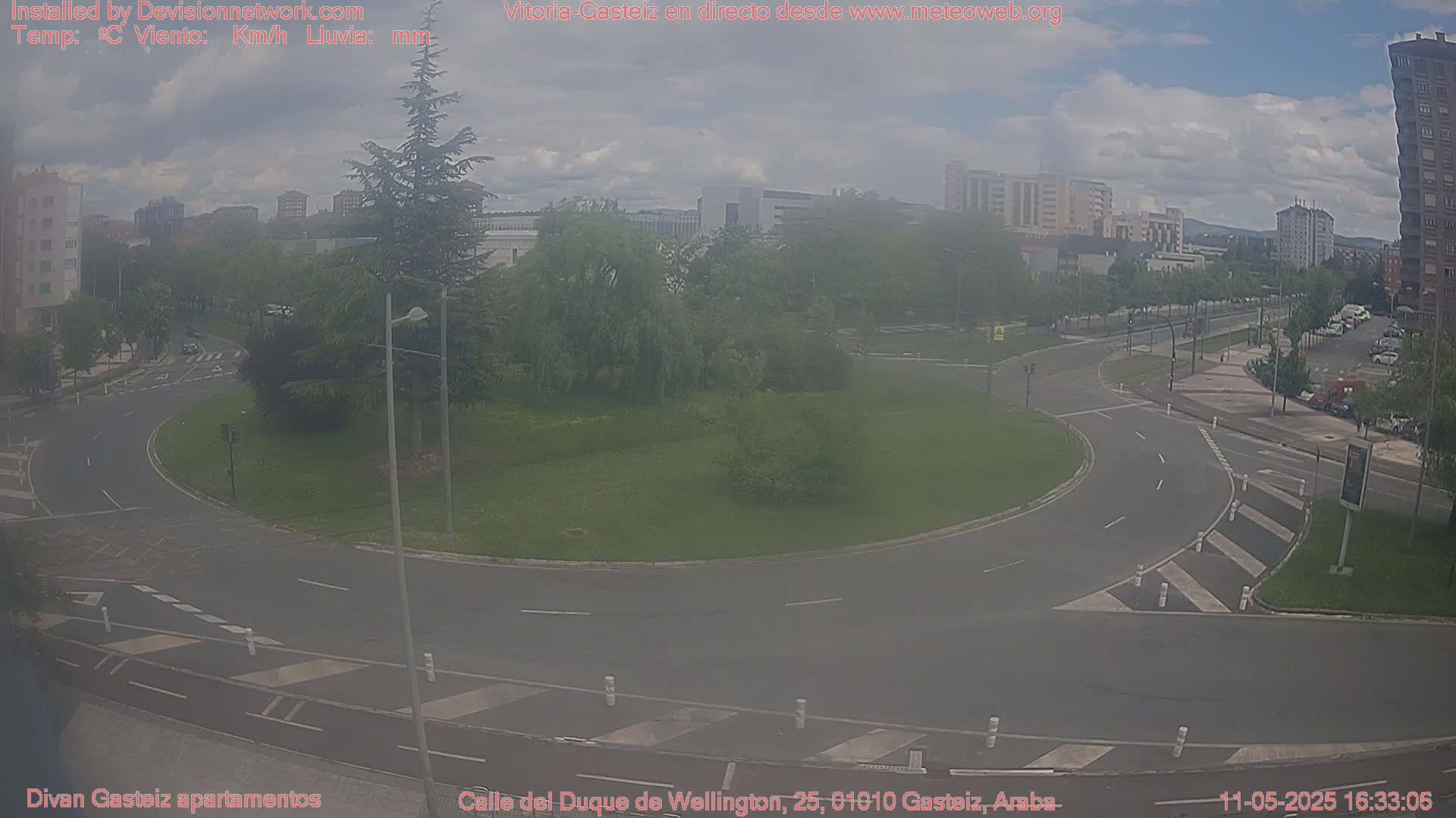 A hazy view of a roundabout in a city, surrounded by buildings, trees, and overcast skies.