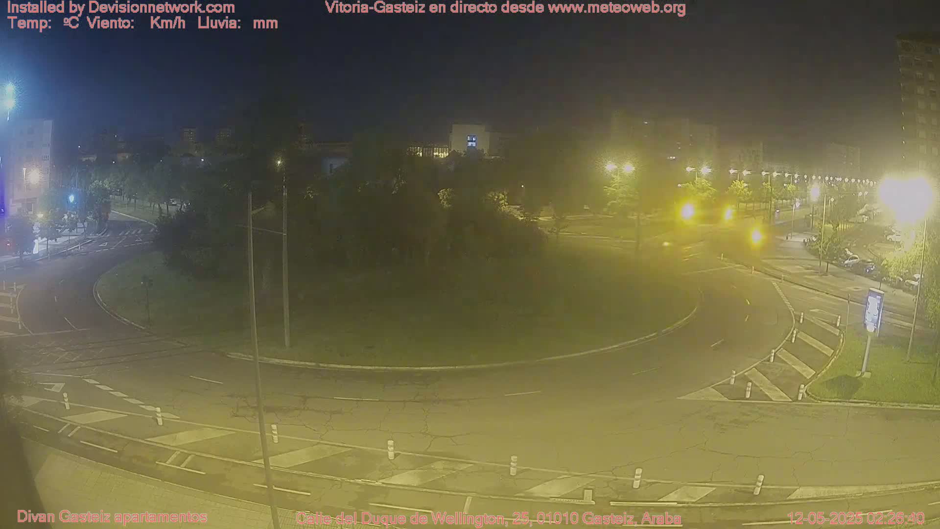 A nighttime view of a traffic roundabout with surrounding buildings and streetlights under hazy conditions.