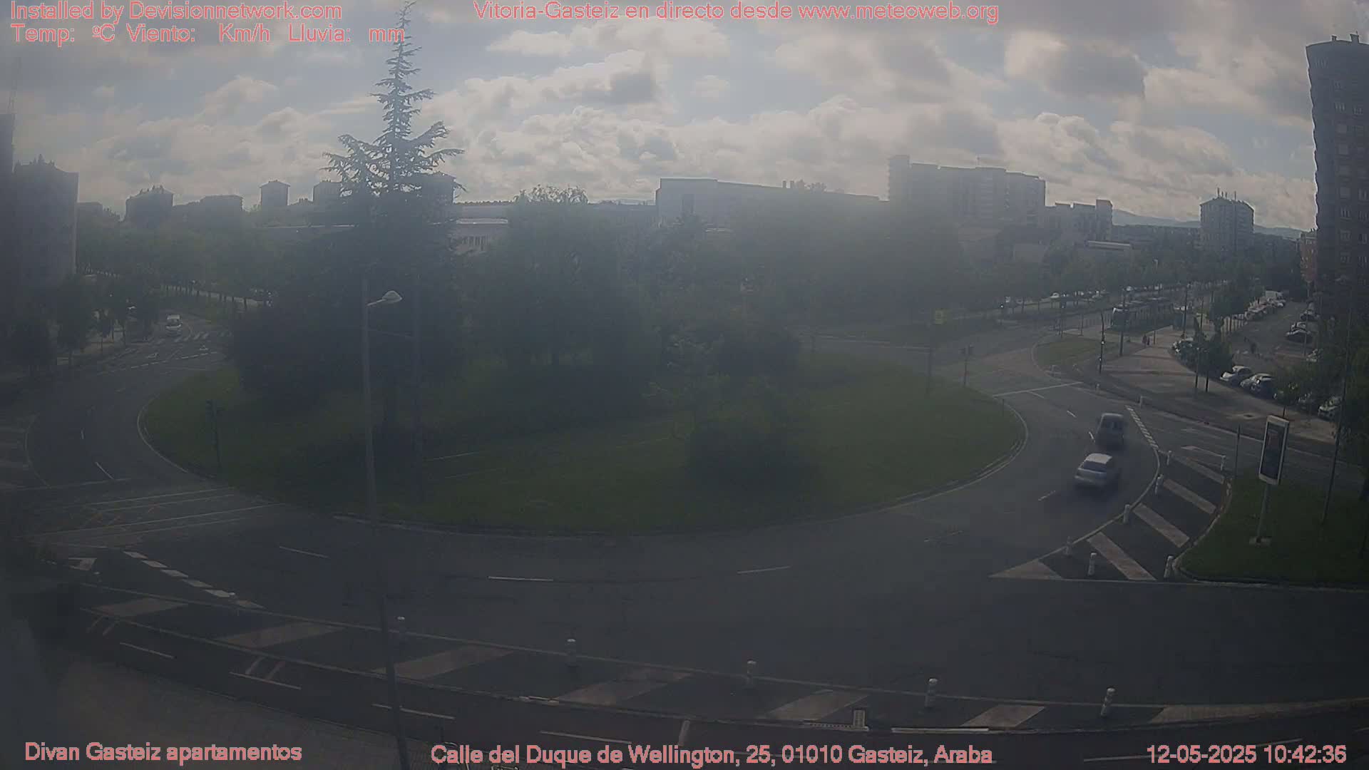 A hazy, partly cloudy day overlooks a roundabout in a city with several cars visible on the roads.