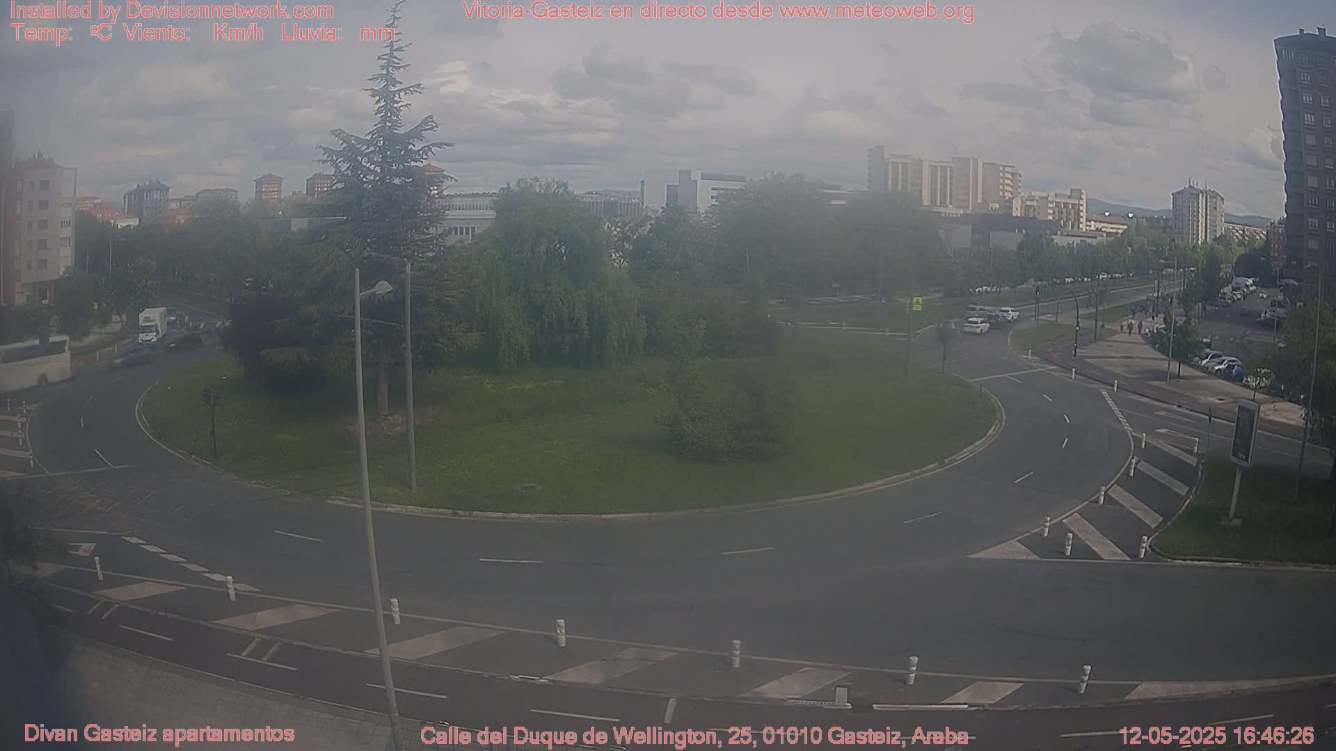 A hazy, overcast day reveals a roundabout surrounded by green space and apartment buildings, with cars moving along a roadway.