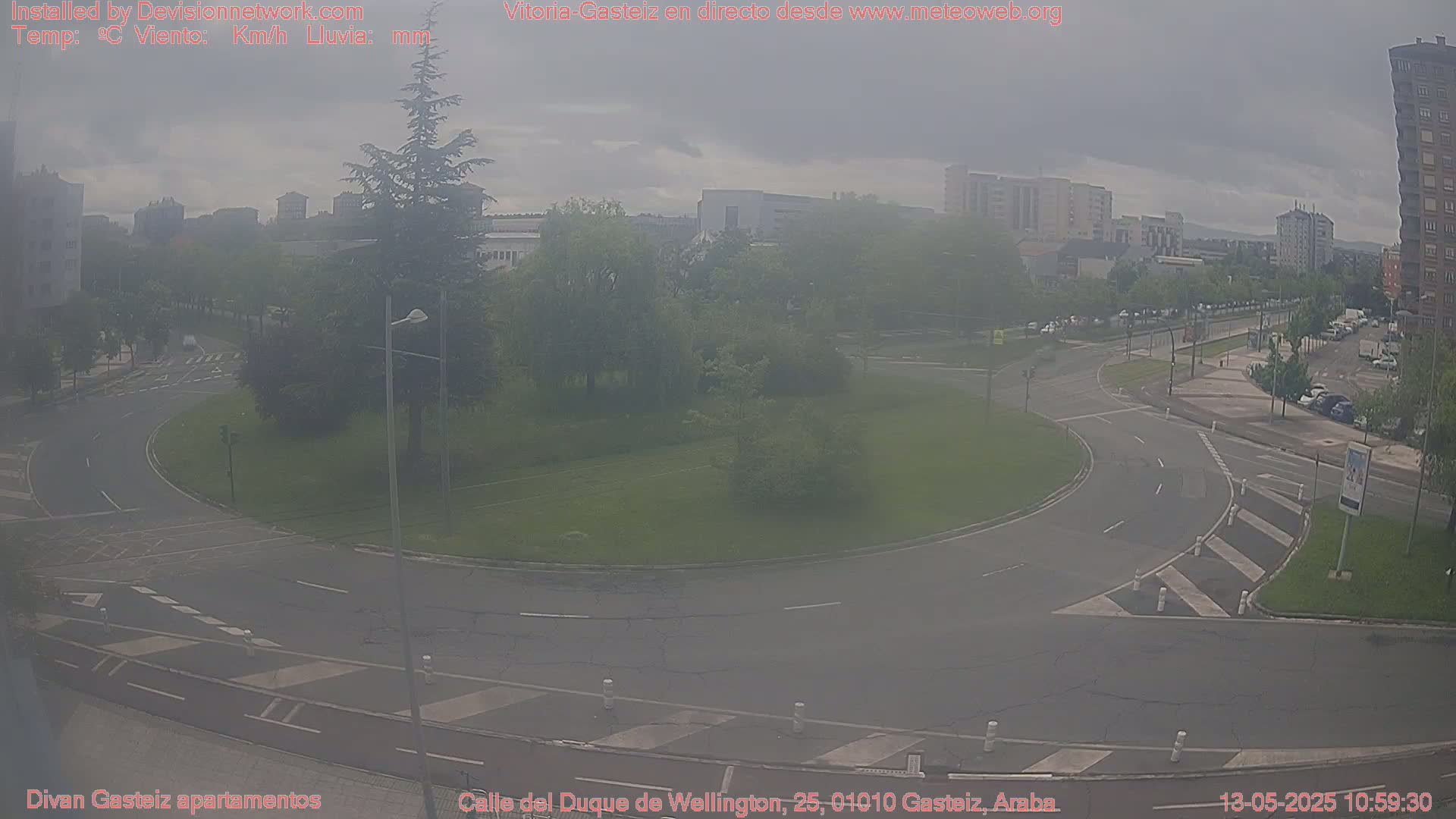 A hazy view of a roundabout in a city, with cars and buildings visible in the background under a cloudy sky.