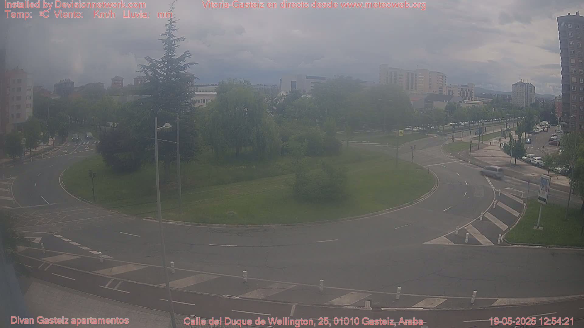 A hazy view of a roundabout in a city with several buildings in the background under overcast skies.