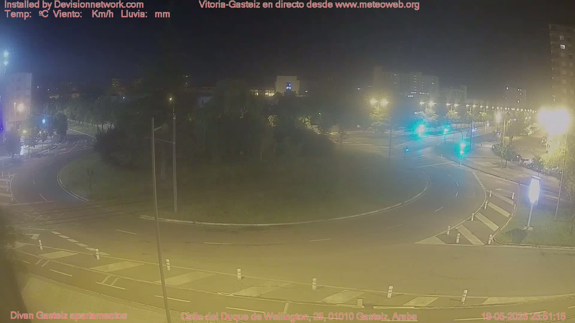 A nighttime, low-light view of a roundabout in a city, with a few cars visible on the road.