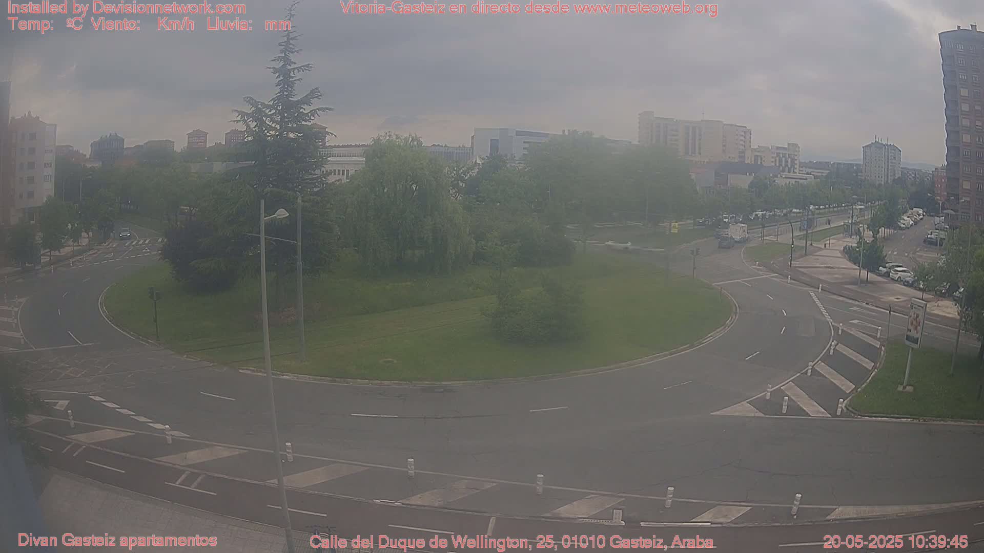 A hazy, overcast day reveals a roundabout surrounded by a grassy area and city buildings.