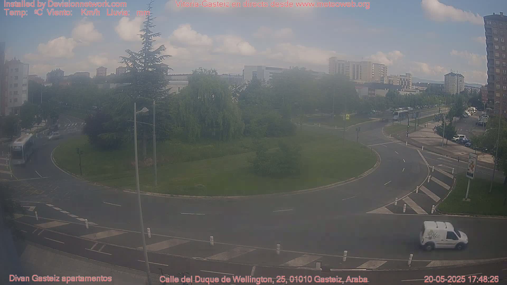 A hazy view of a roundabout in a city, with several vehicles visible, under a partly cloudy sky.