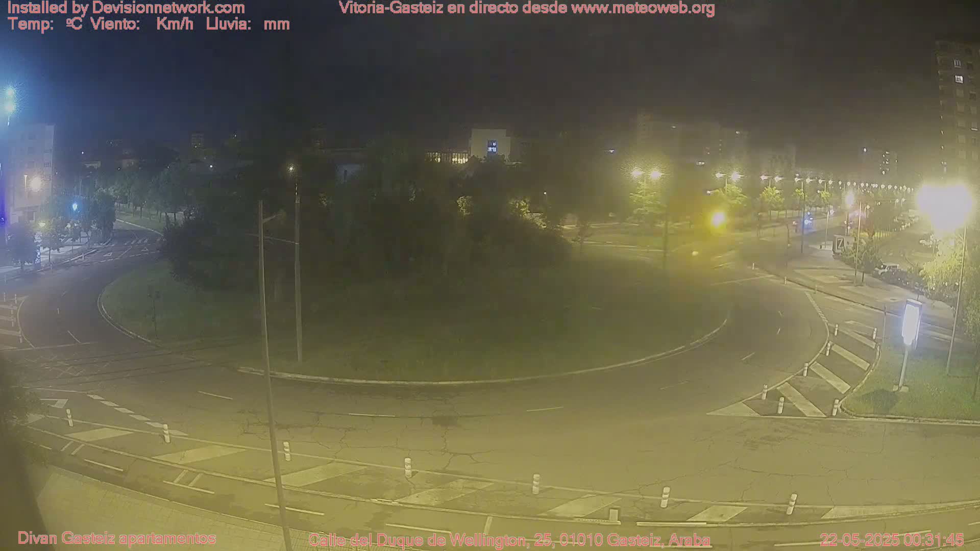 A nighttime view of a roundabout in a city with streetlights illuminating the roadway and surrounding buildings.