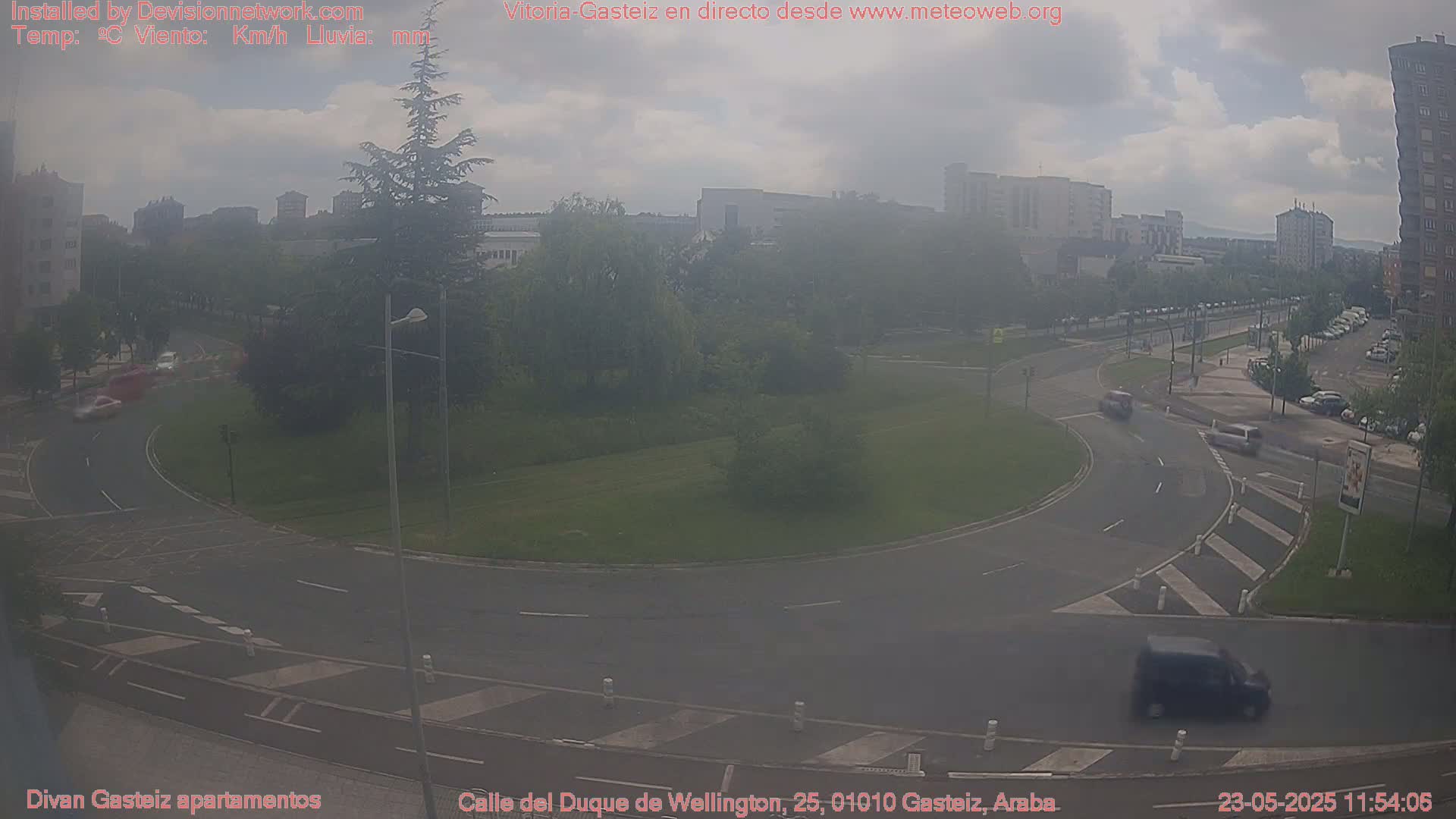 A hazy, overcast day shows a roundabout with several cars driving through it and buildings in the background.