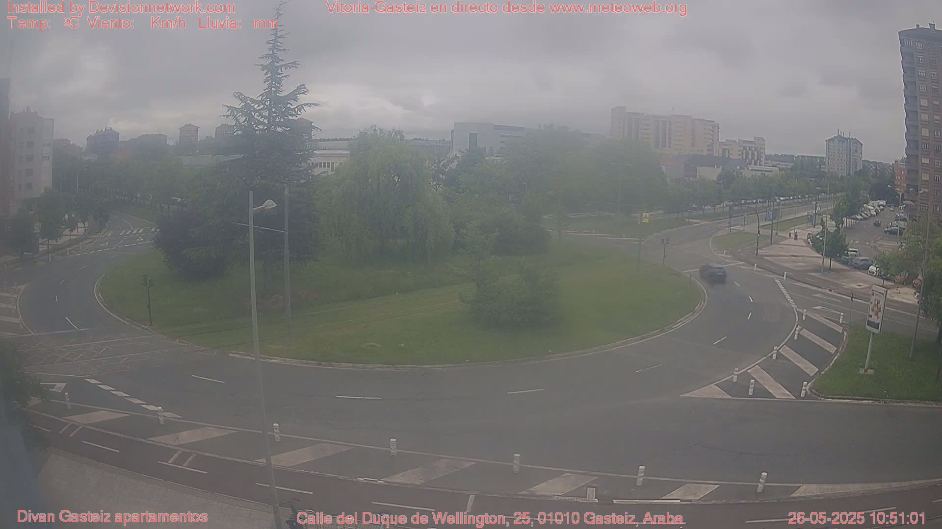 A hazy view of a roundabout and surrounding city streets, with buildings and trees visible in the distance.