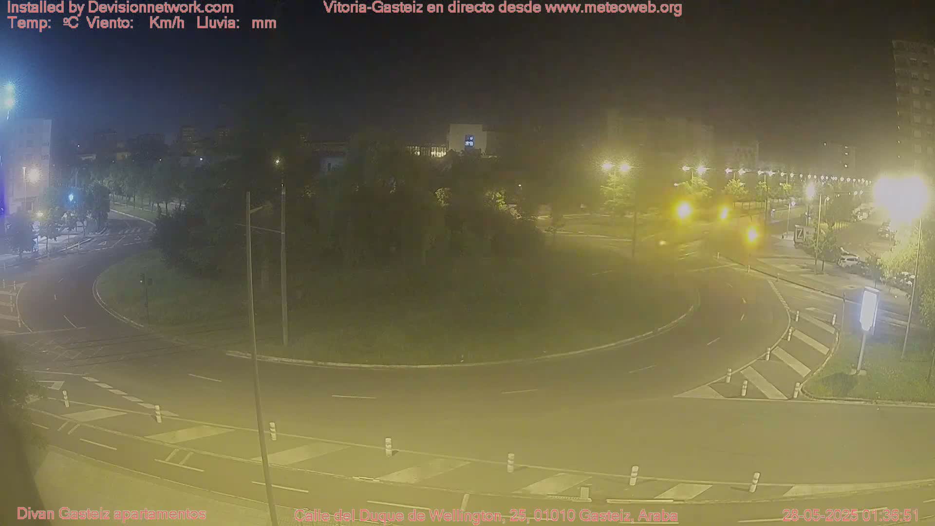 A nighttime, dimly lit view of a roundabout in a city, with a few cars visible.