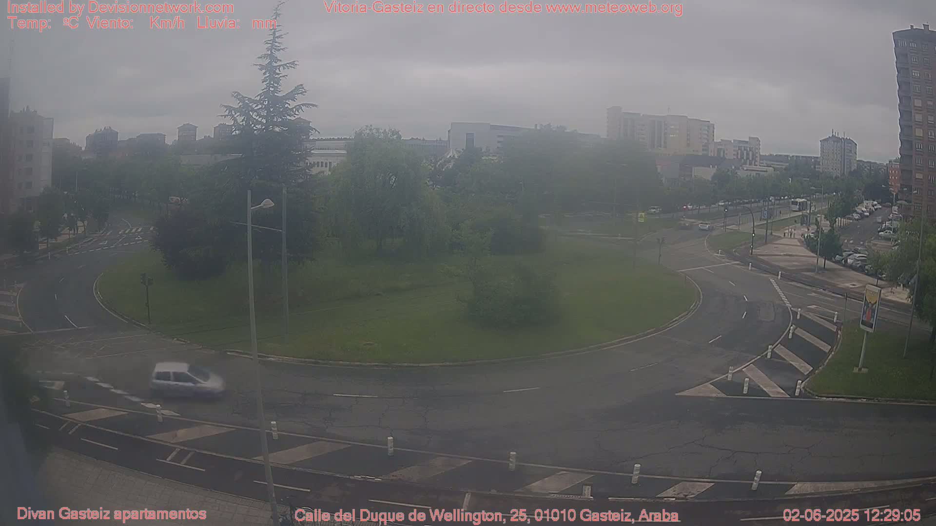 A hazy, overcast view of a roundabout and surrounding city streets with a few cars, trees, and buildings visible in the distance.