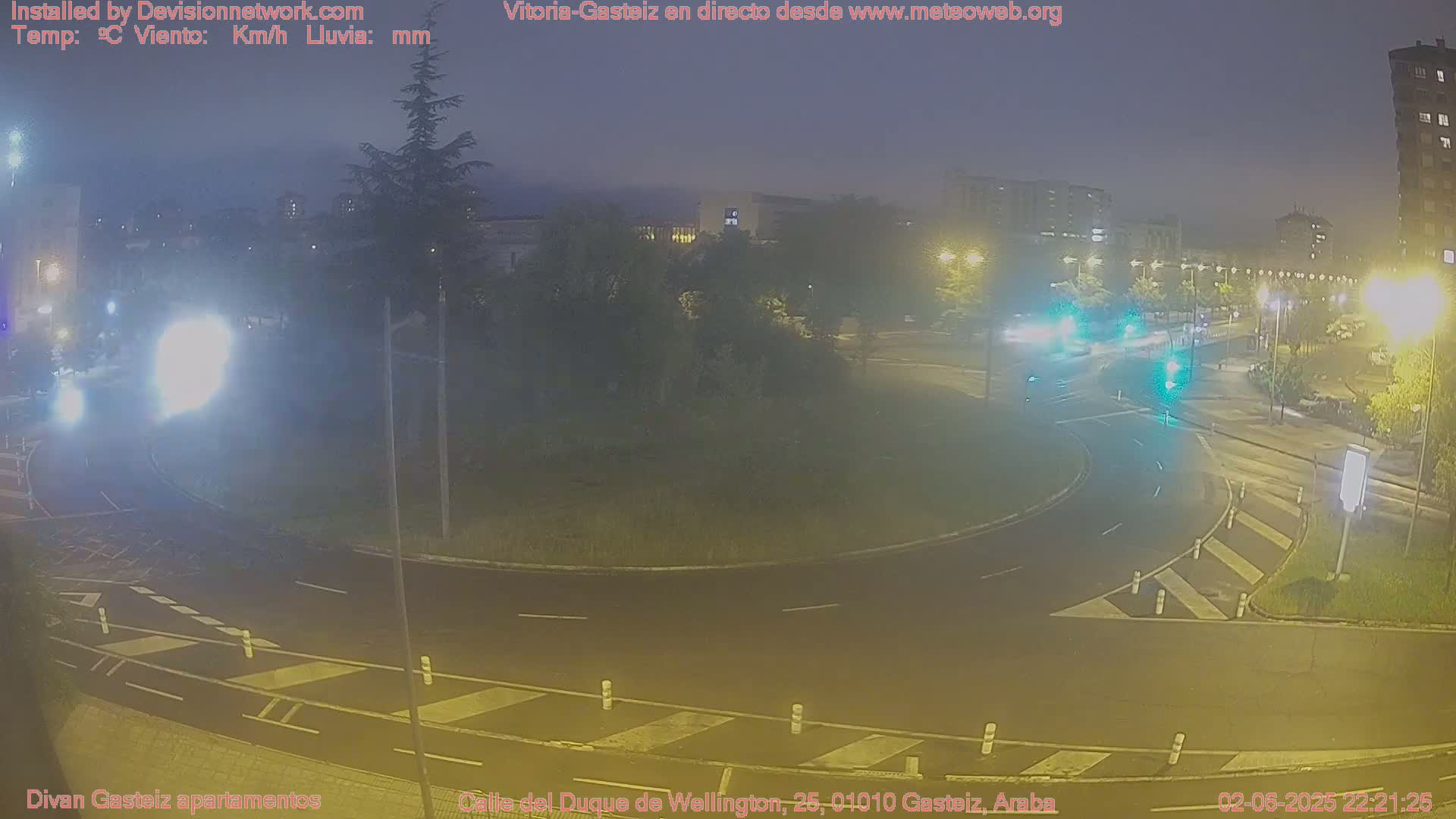 A nighttime view of a roundabout with cars and streetlights, under hazy conditions.