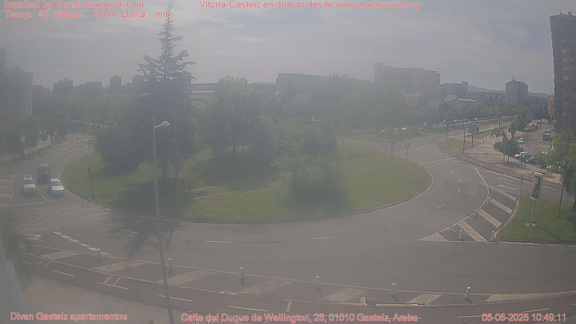 A hazy view of a roundabout and surrounding streets with several cars visible, under a mostly clear sky.
