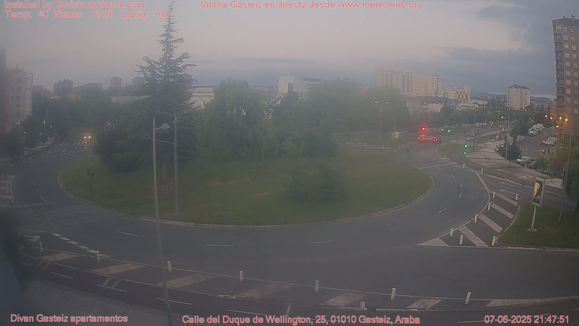 A hazy, overcast view of a roundabout surrounded by trees and buildings, with several cars visible on the roads.