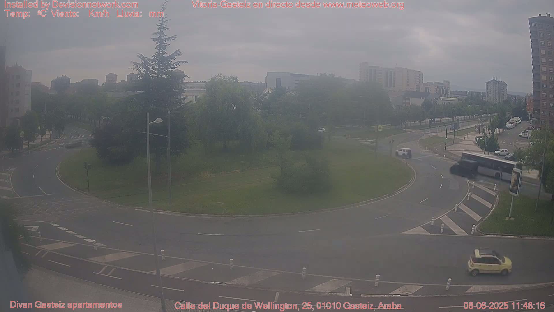A hazy, overcast day shows a roundabout in a city with several cars and a bus driving around it.