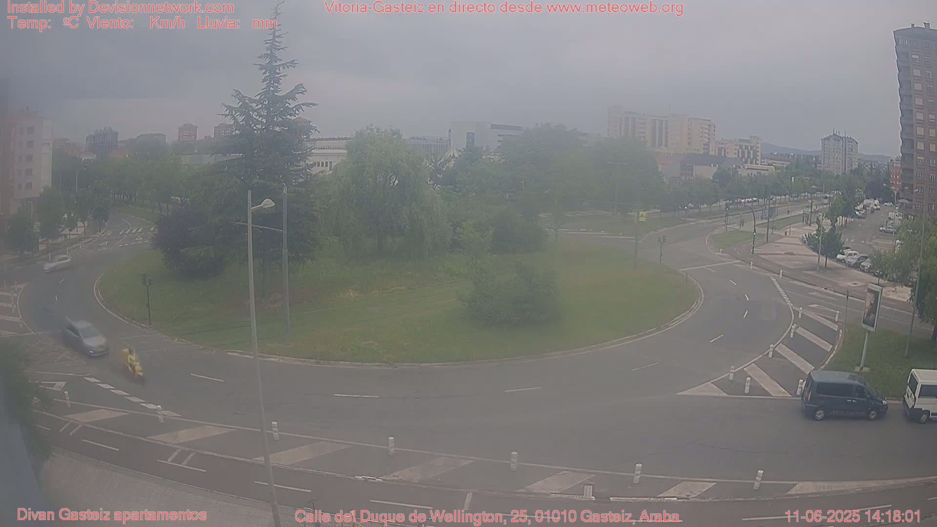 A hazy view of a roundabout and surrounding streets in a city, with several vehicles visible.