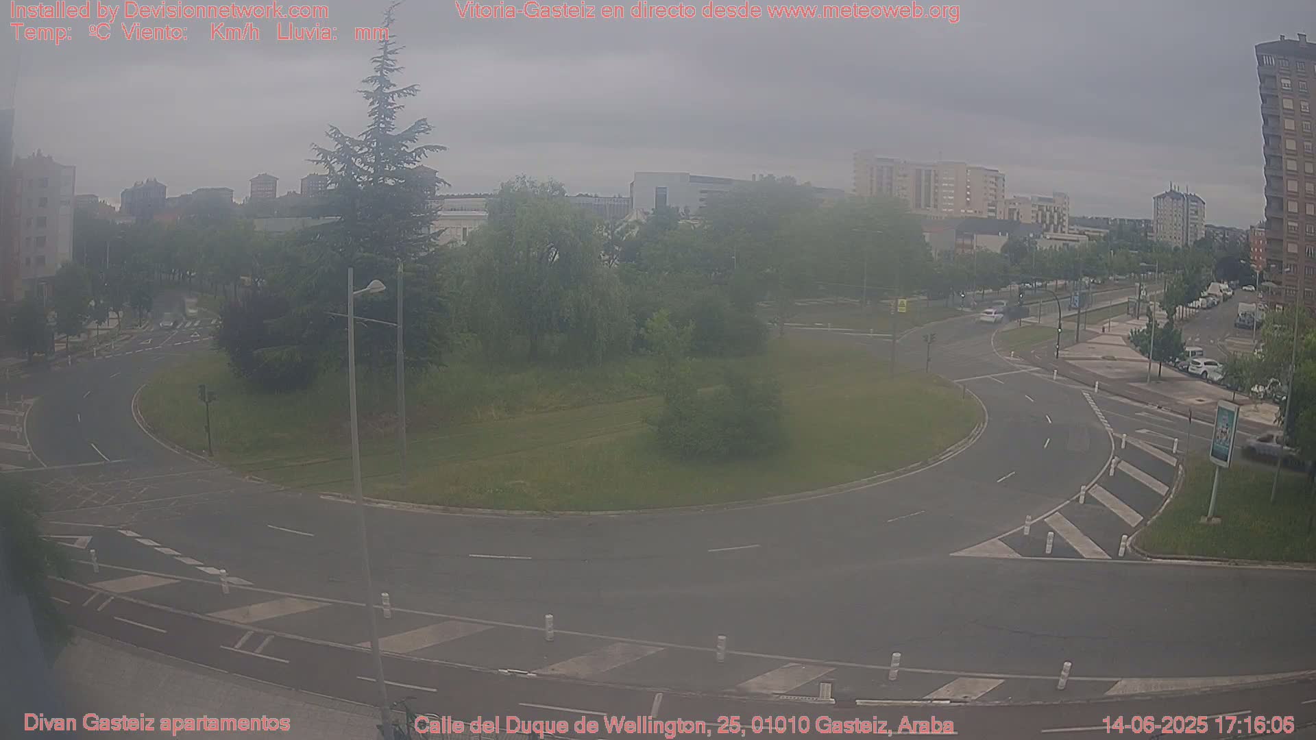 A hazy overcast day reveals a roundabout in a city with surrounding buildings and green spaces.