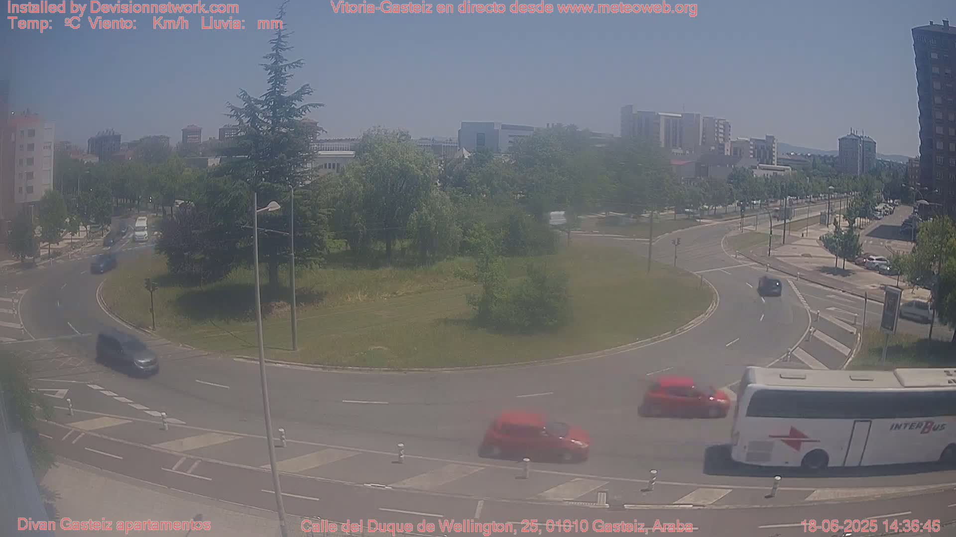 A traffic roundabout with several cars and a bus, situated in a city on a sunny day.