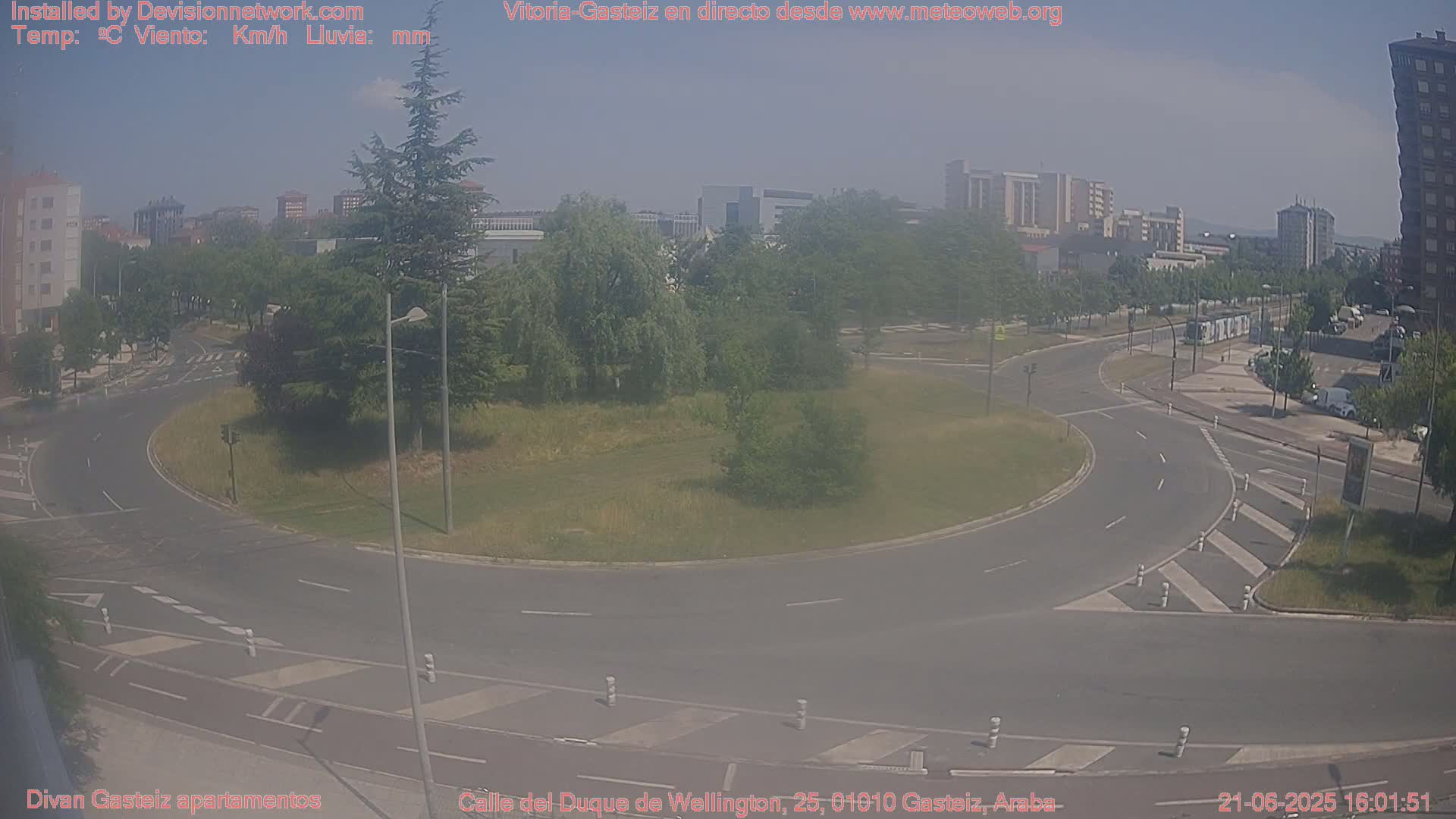 A hazy, sunny day shows a roundabout surrounded by roads, buildings, and trees.