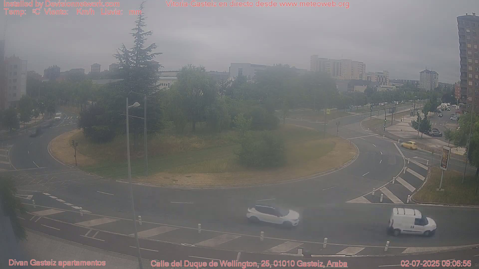A hazy view of a roundabout and surrounding roads in a city, with several cars and a van visible.