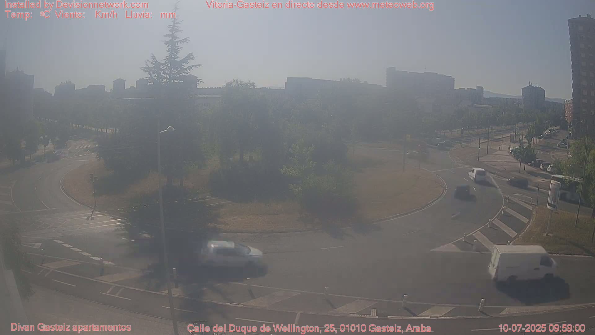 A hazy, sunny day shows a roundabout with several vehicles and buildings in the distance.