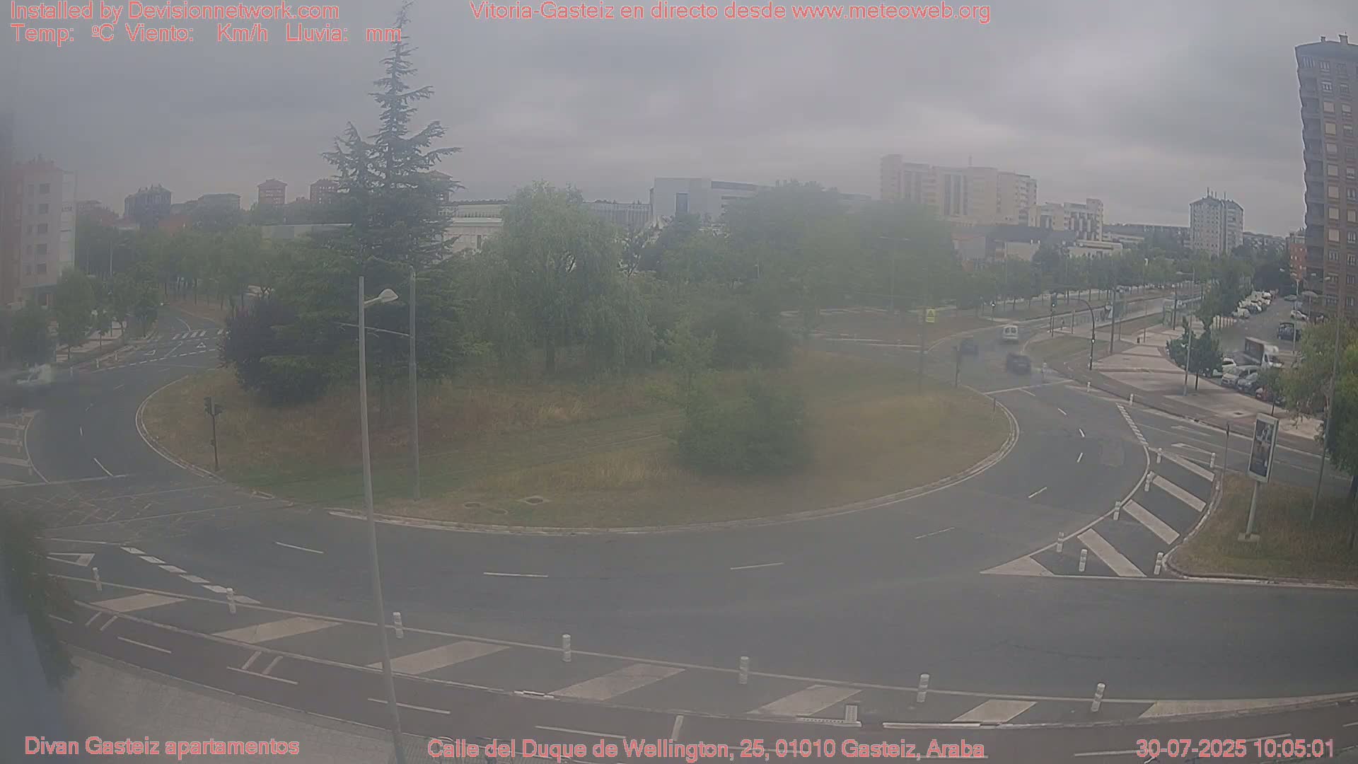 A hazy, overcast day reveals a roundabout surrounded by greenery and buildings, with a few cars visible on the roads.