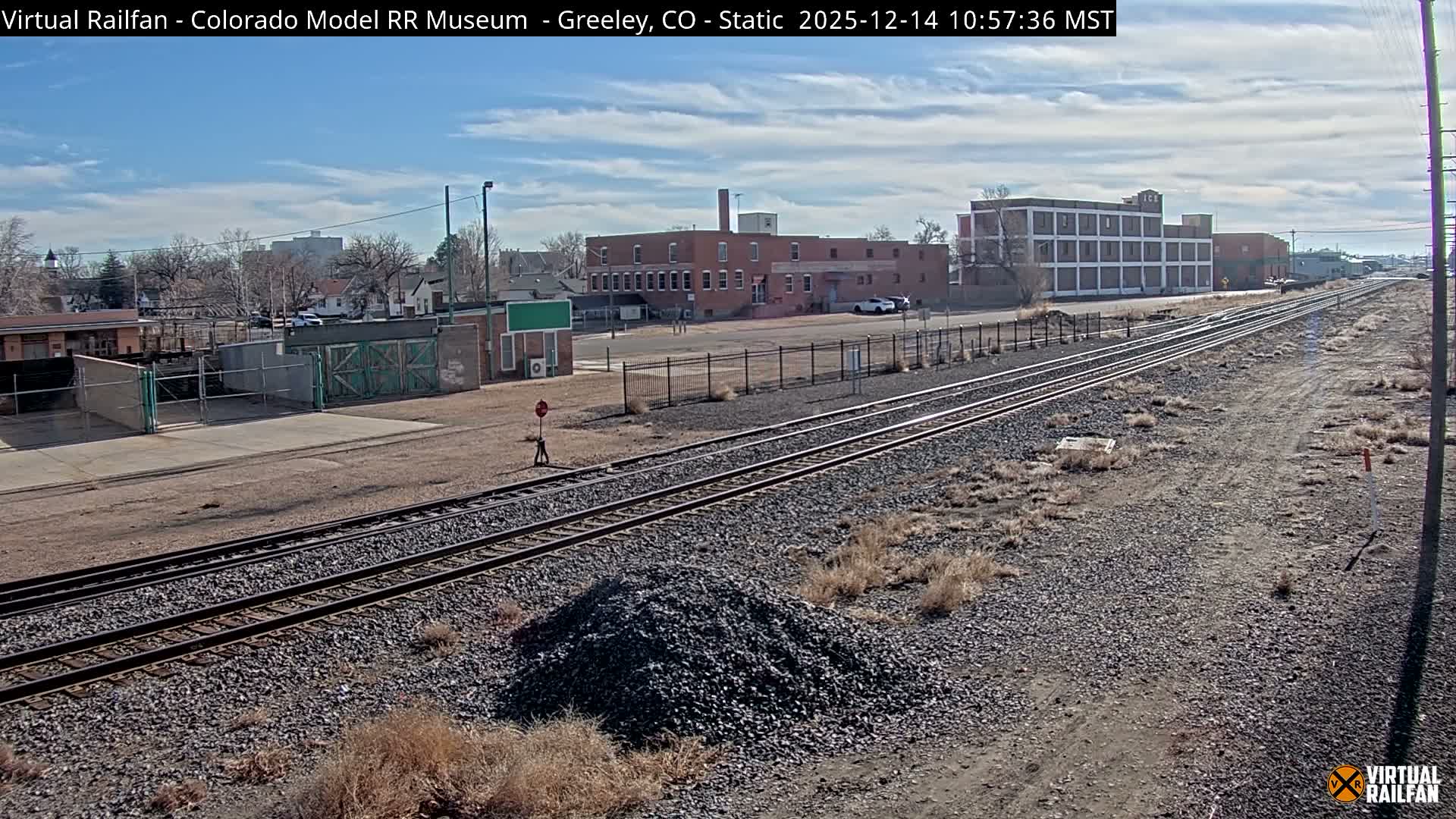 A nighttime view reveals a snowy railway yard with multiple tracks, flanked by illuminated industrial buildings and factories emitting plumes of steam into the cold, dark sky.