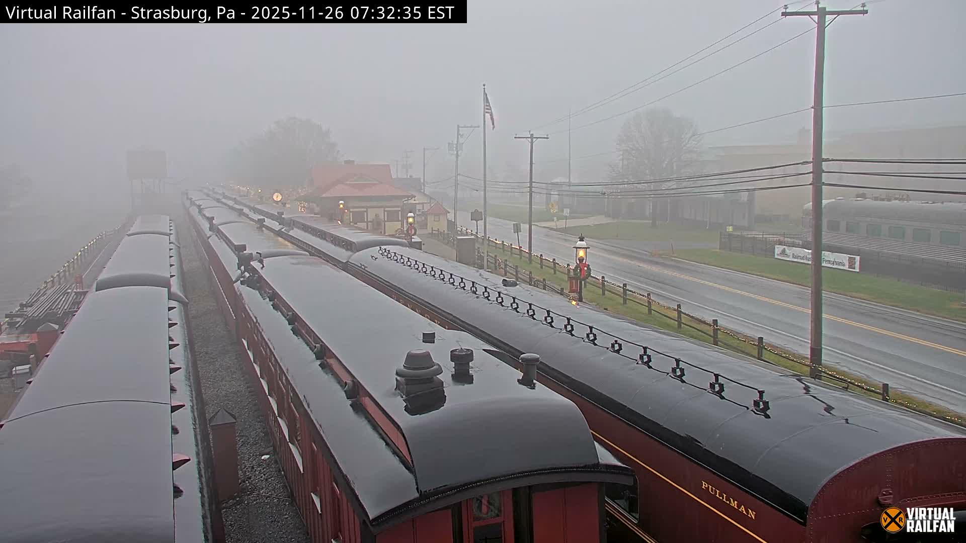 The image presents a night scene at a train station under a clear sky, showcasing multiple trains on parallel tracks, brightly lit station buildings, and a long string of decorative lights lining the trackside.