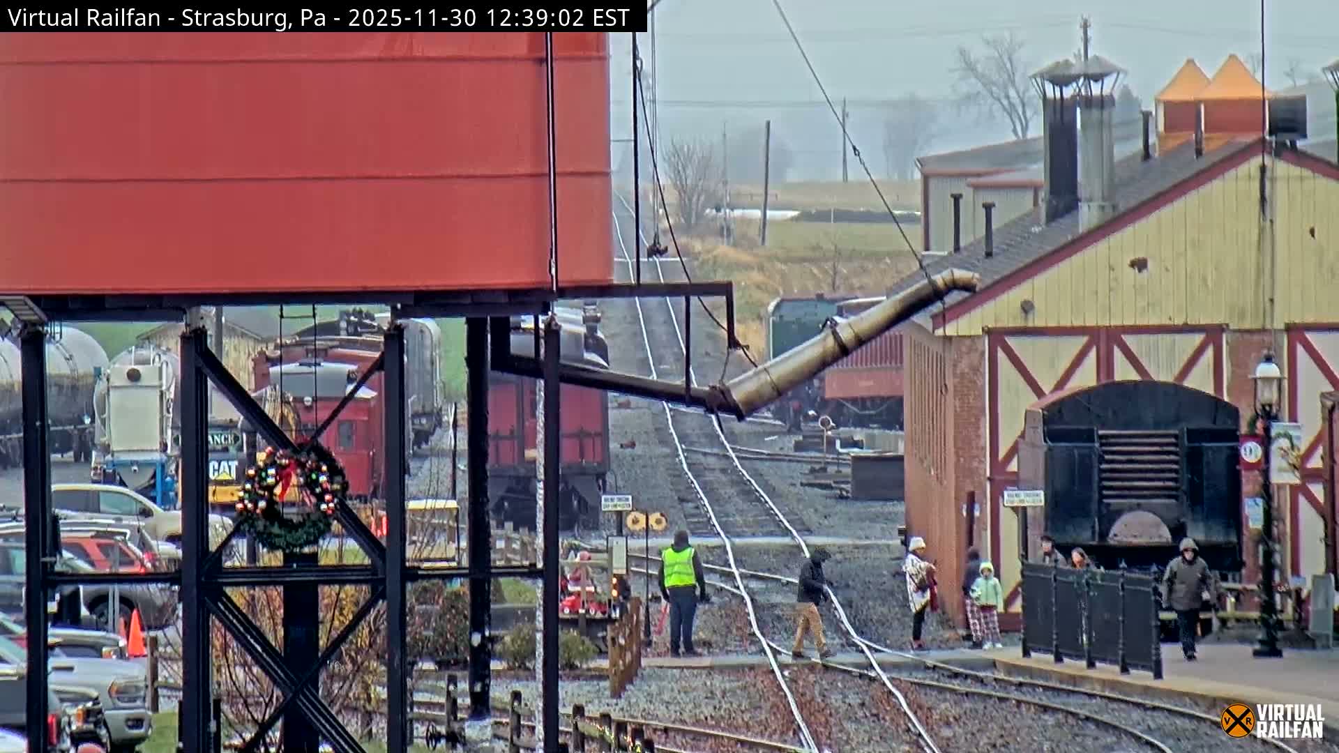 The image presents a night scene at a train station under a clear sky, showcasing multiple trains on parallel tracks, brightly lit station buildings, and a long string of decorative lights lining the trackside.