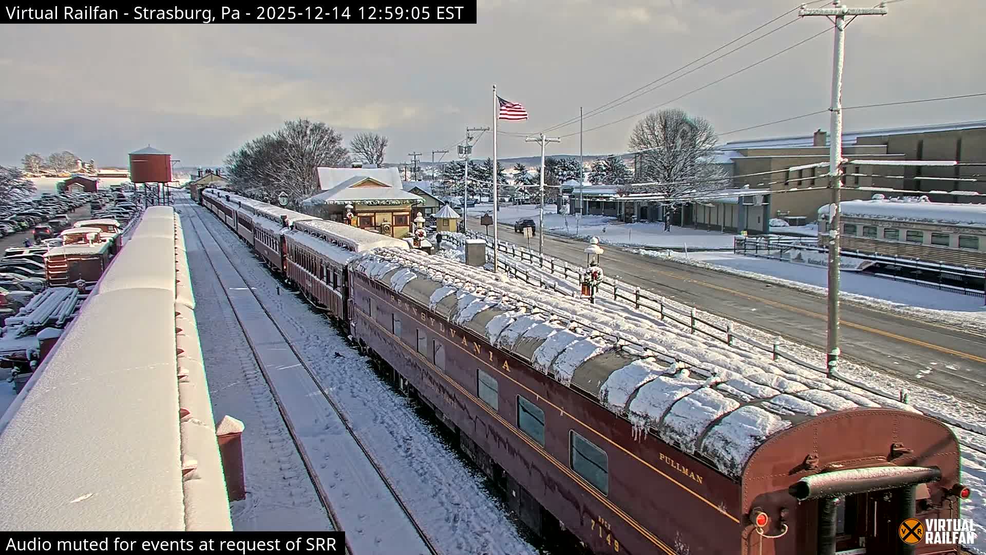 A passenger train with illuminated windows and festive string lights is parked at a brightly lit station under a clear night sky.