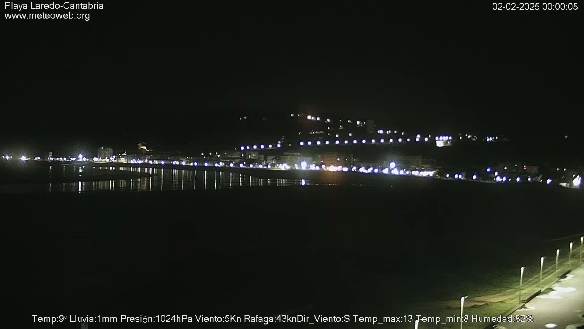 A nighttime view of a dimly lit beach town with a calm body of water reflecting the lights.