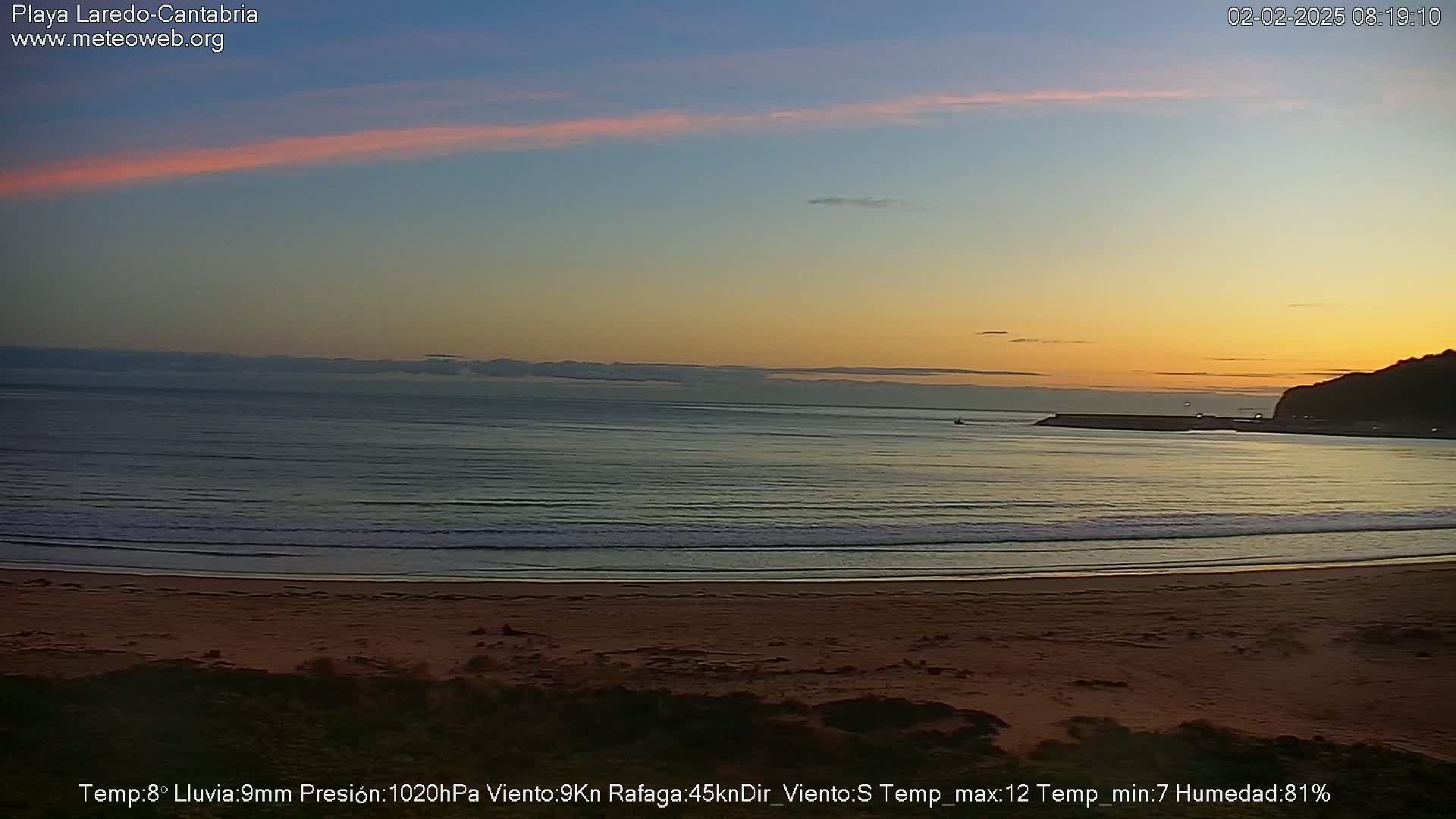 A sandy beach with gentle waves laps at the shore under a sunrise sky.
