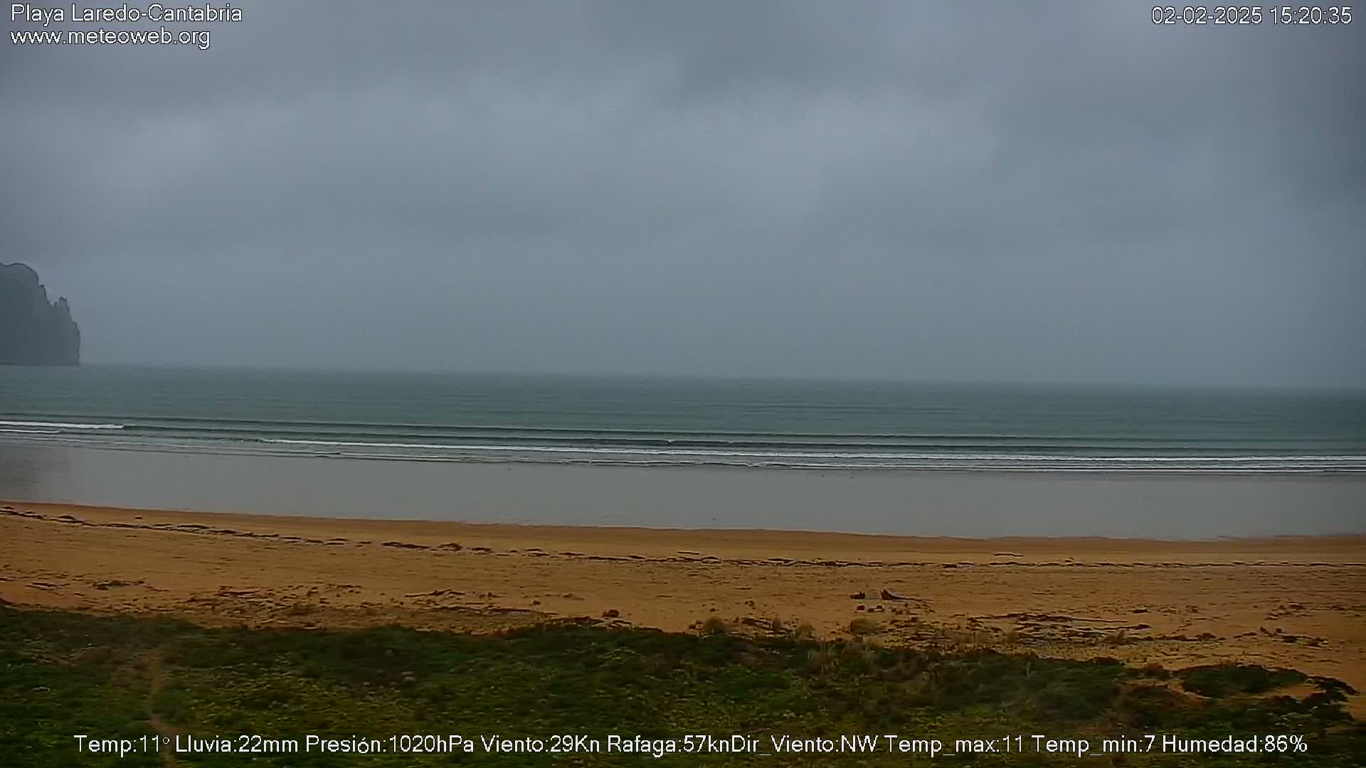 A sandy beach with gently rolling waves under an overcast sky.