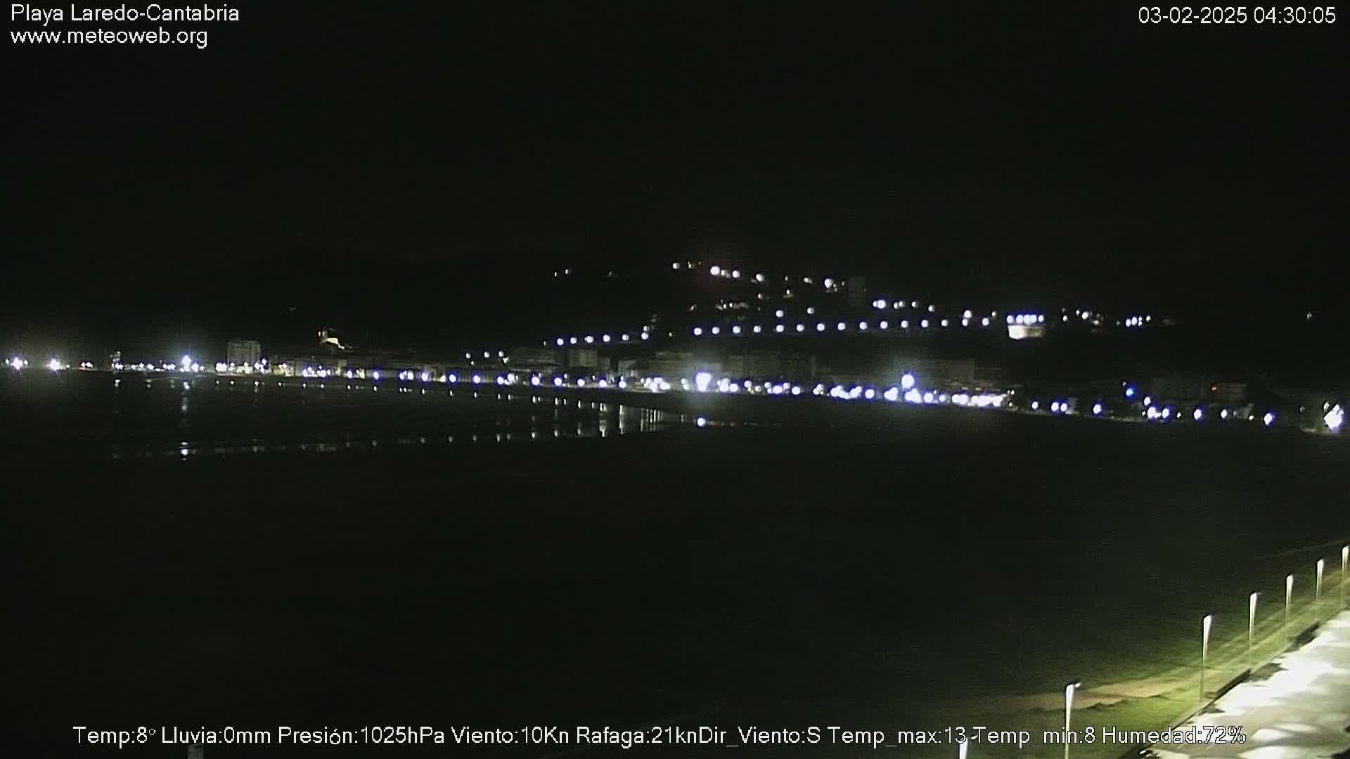 A nighttime long shot of a dark, calm body of water reflecting the lights of a town on the opposite shore.