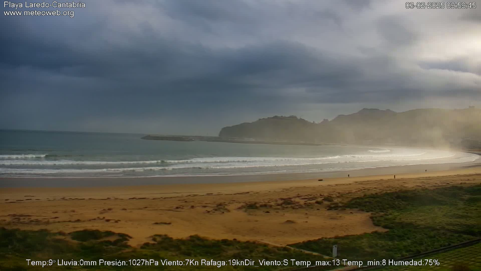 A sandy beach with gentle waves under a cloudy sky.