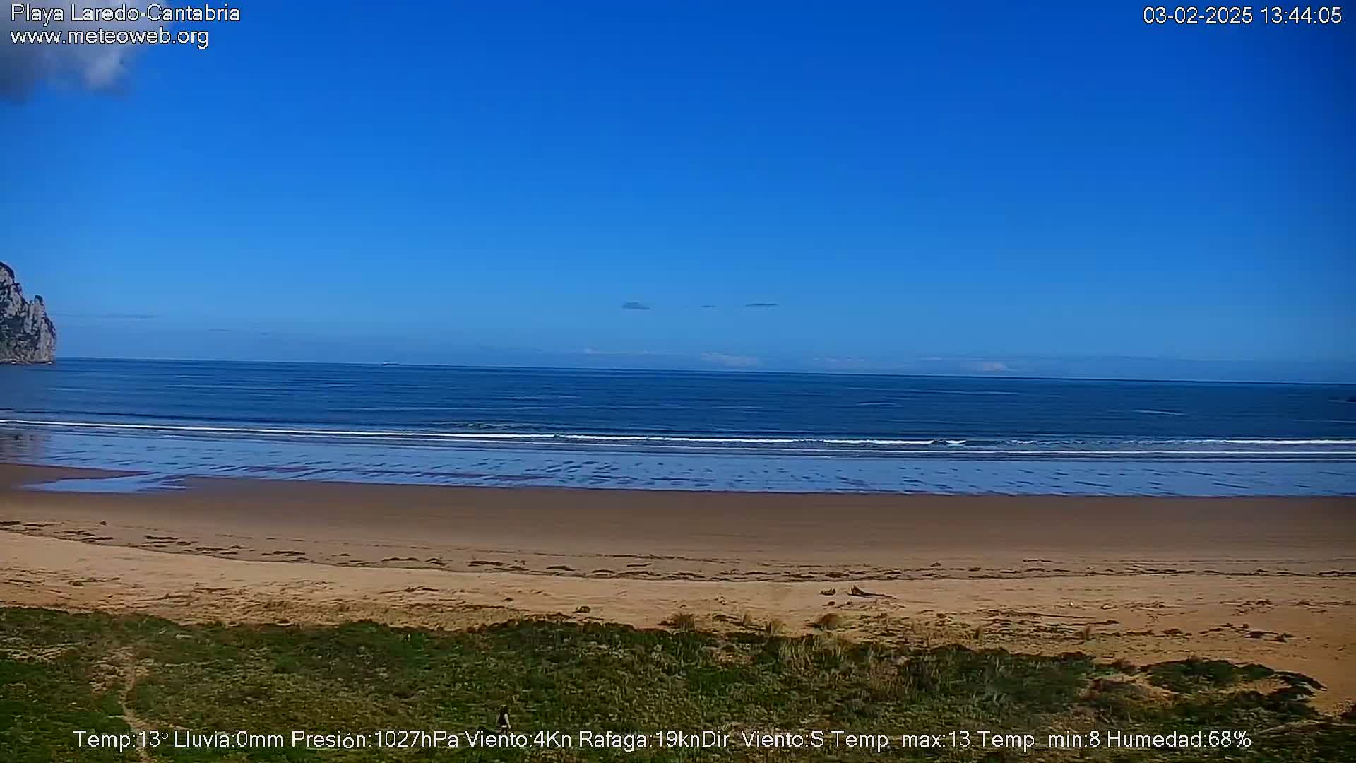 A sandy beach stretches to a calm ocean under a clear blue sky.