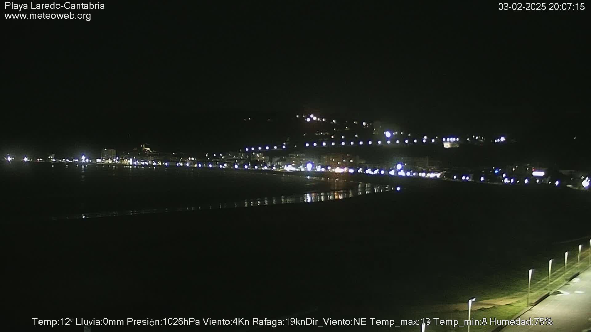 A nighttime view of a dimly lit beach town and coastline under clear skies.