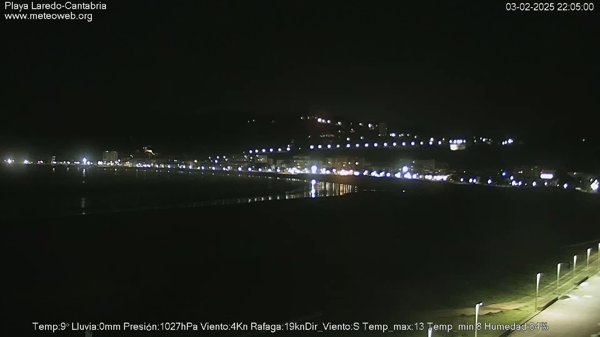 A nighttime view of a dimly lit coastal town and beach, under a clear sky.