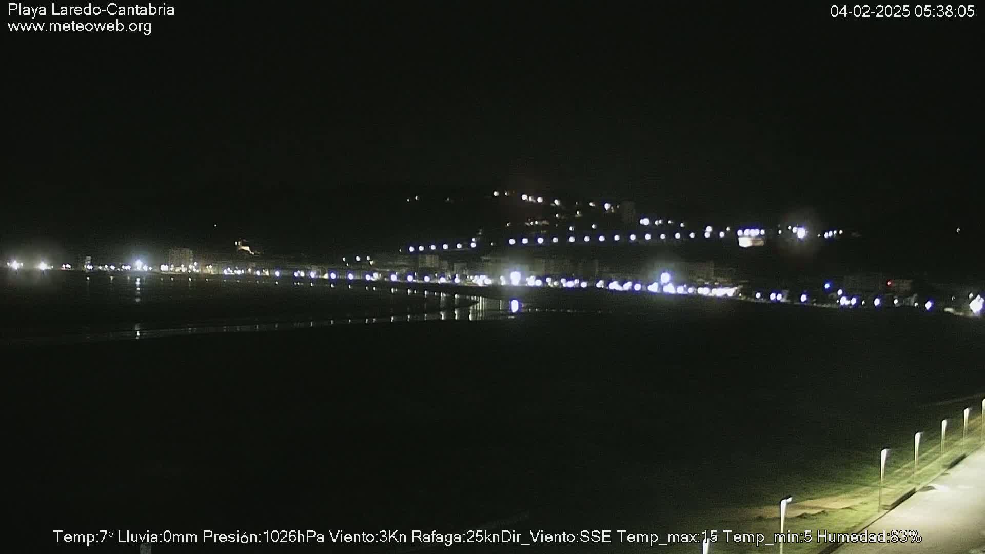 A nighttime view of a dark beach and a town illuminated by lights under a clear, dark sky.