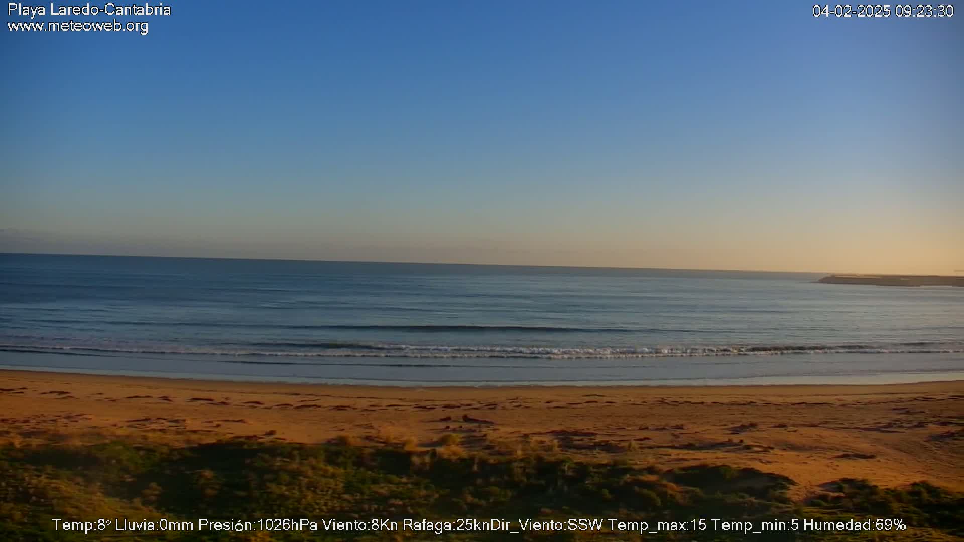 A sandy beach meets a calm ocean under a clear blue sky.