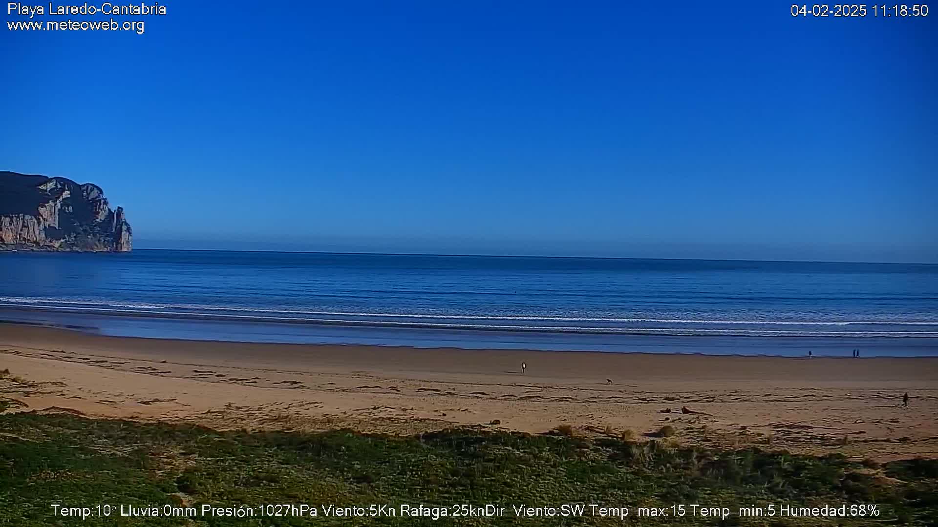 A sandy beach stretches to a calm ocean under a clear blue sky, with a rocky cliff visible in the distance.